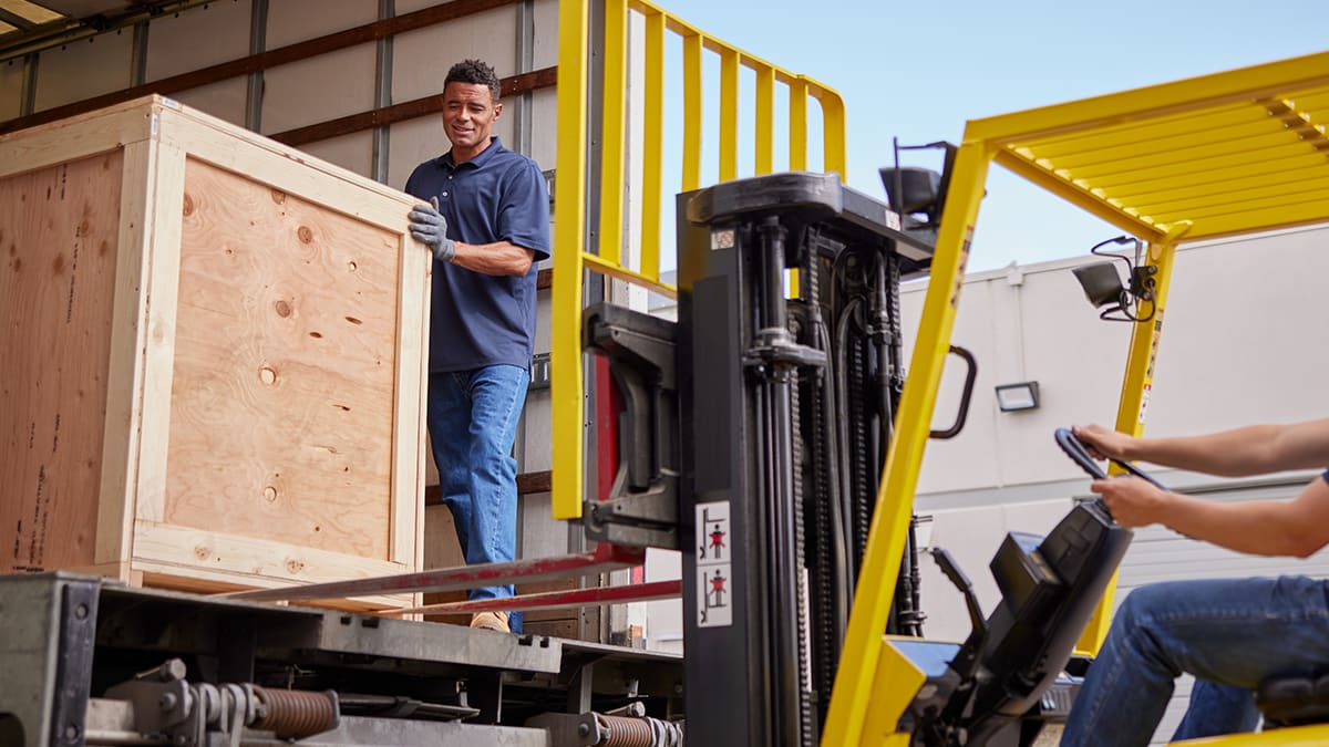 A large wooden freight crate being loaded into a truck with a forklift.