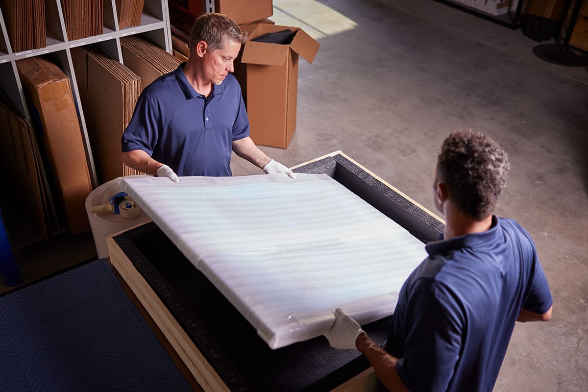 Pak Mail team members protecting a crated shipment with foam padding.